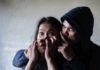 Man holding womans mouth gesturing silence