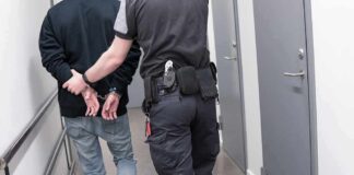 Officer escorting handcuffed person down hallway