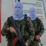 Masked soldiers holding rifles in front of a monument