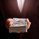 Hand holding a stack of hundred-dollar bills