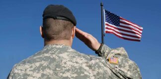 Soldier in military uniform saluting in front of an American flag
