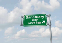 Green road sign saying sanctuary city next exit