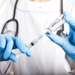Doctor filling syringe with vaccine from vial.