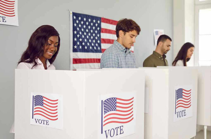 People voting in booths with American flag backdrop.