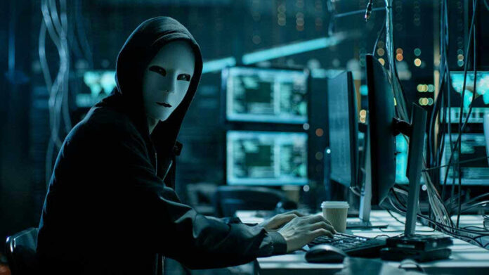 Person wearing mask and hoodie at computer desk