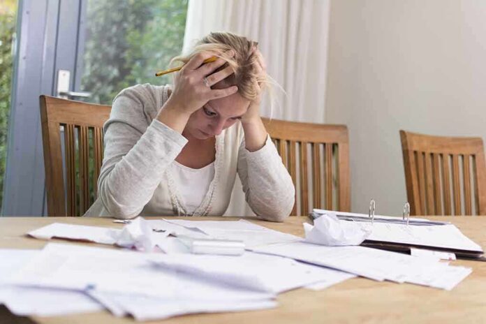 A woman sitting at a desk with her head in her hands, surrounded by paperwork