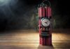 A stick of dynamite with a clock timer and wires, set against a dark smoky background