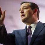 Man in suit raising his hand while speaking.