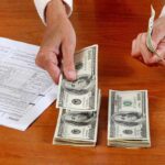 Hands counting cash and reviewing financial documents on a wooden table