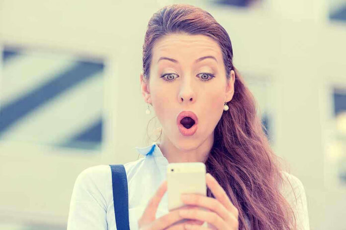 Surprised woman looking at her smartphone outdoors