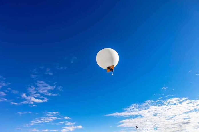 A white balloon floating in a clear blue sky with scattered clouds