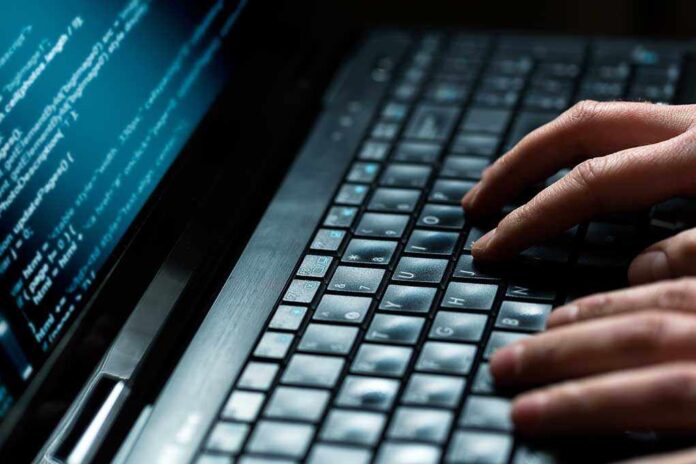 Close up of hands typing on a laptop keyboard with code displayed on the screen