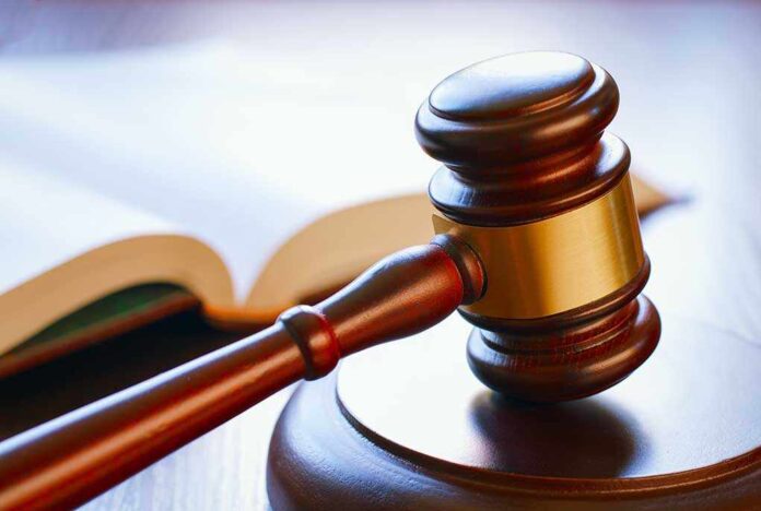 A wooden gavel resting on a round base with an open law book in the background