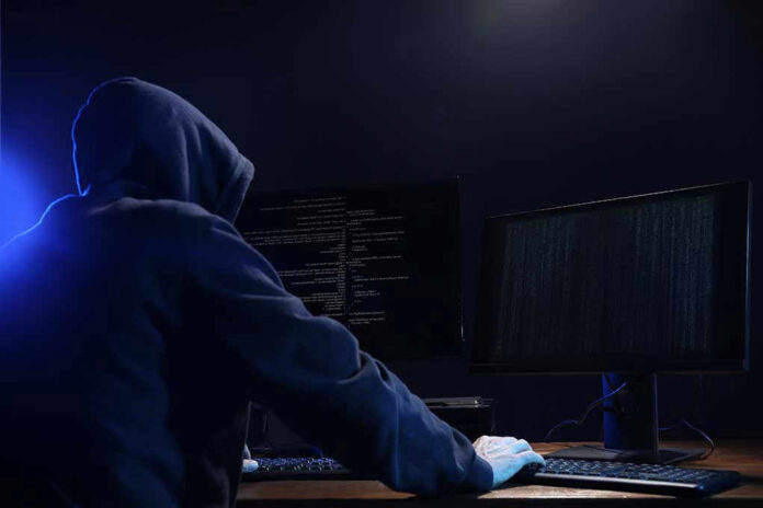 Hooded figure using dual monitors in dark room