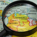 Airspace CLOSED — Trump Shuts Down Venezuela Magnifying glass focusing on Venezuela and Colombia on map.