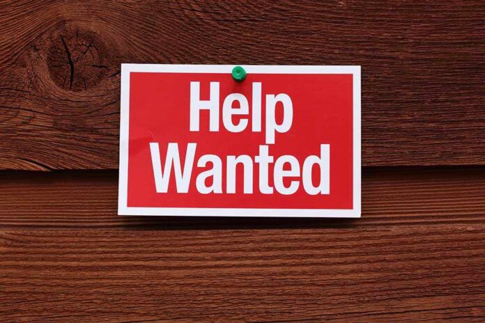 A red and white Help Wanted sign pinned to a wooden surface