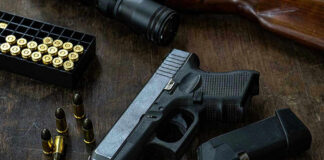 Handgun with ammunition, magazine, and rifle on wooden table.