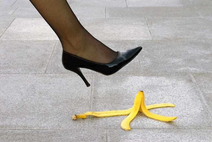 A high heel shoe poised above a banana peel on a tiled floor
