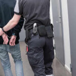 Lawmaker’s SICKENING Double LIFE Officer escorting handcuffed person down hallway.