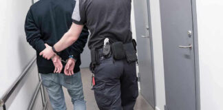 Officer escorting handcuffed person down hallway.