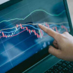 Trump Creates MASSIVE PLUMMET — Unseen in 50 Years Hand pointing at stock market graph on laptop.