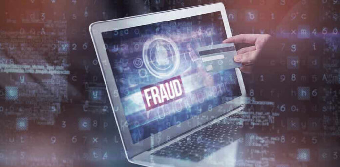 Person holding credit card near laptop displaying Fraud.