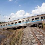 Crane CRASHES on Train—32 Dead! An overturned train on a railway track surrounded by vegetation