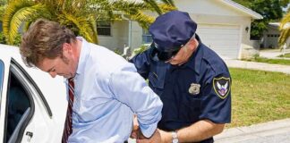 A police officer handcuffing a man in formal attire outside a police car
