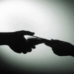 $35,000 Servicemen Betrayal – China Infiltrates U.S. Bases Silhouette of hands exchanging money in dim light.