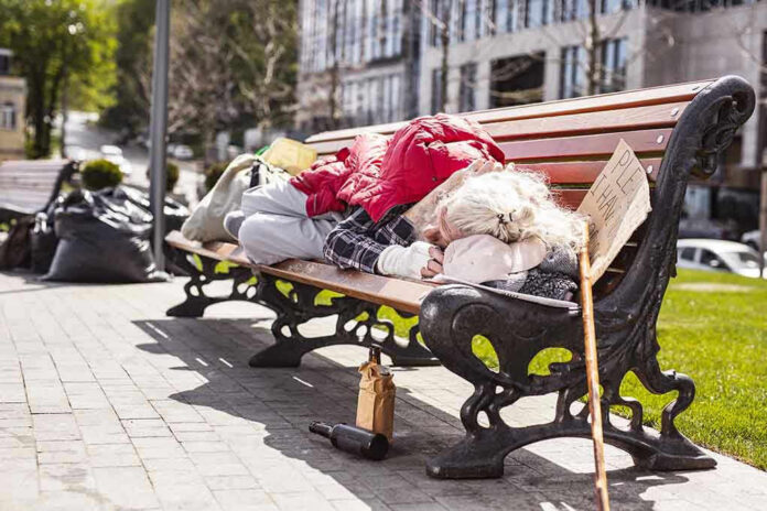 Person sleeping on park bench with cardboard sign.