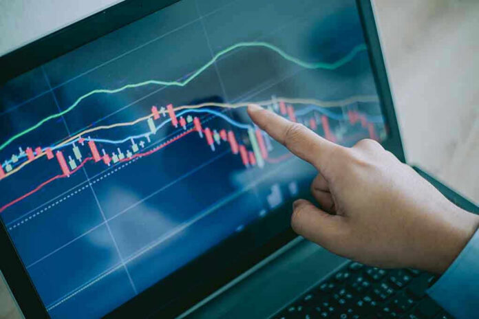 114313067 Hand pointing at stock market graph on laptop screen.