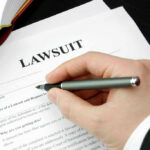 Hand holding pen, filling out lawsuit form.