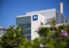 Modern hospital building with a prominent H sign against a clear blue sky
