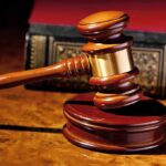 Media Tycoon SENTENCED TO DIE Behind Bars A wooden gavel resting on a polished surface with a law book in the background