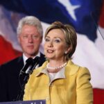 Hillary Clinton delivering a speech with Bill Clinton in the background