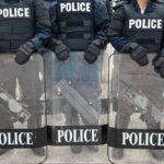 Police officers in riot gear holding shields.