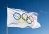 Olympic flag waving against clear blue sky.