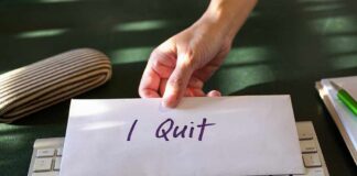A hand placing an envelope labeled 'I Quit' on a keyboard