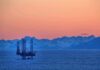 An oil rig in the ocean with a backdrop of mountains during sunset