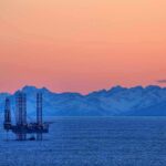 Trump Overrides California—Oil Flows Again! An oil rig in the ocean with a backdrop of mountains during sunset