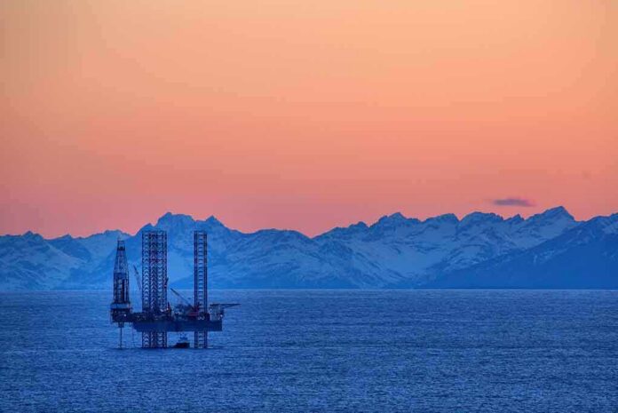 An oil rig in the ocean with a backdrop of mountains during sunset