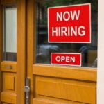 A door with a Now Hiring sign and an Open sign