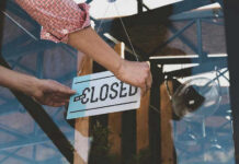 Hand placing closed sign on glass door