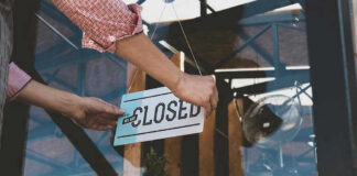 Hand placing closed sign on glass door