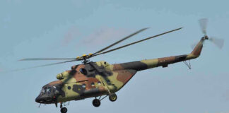 Camouflage military helicopter in flight against blue sky.