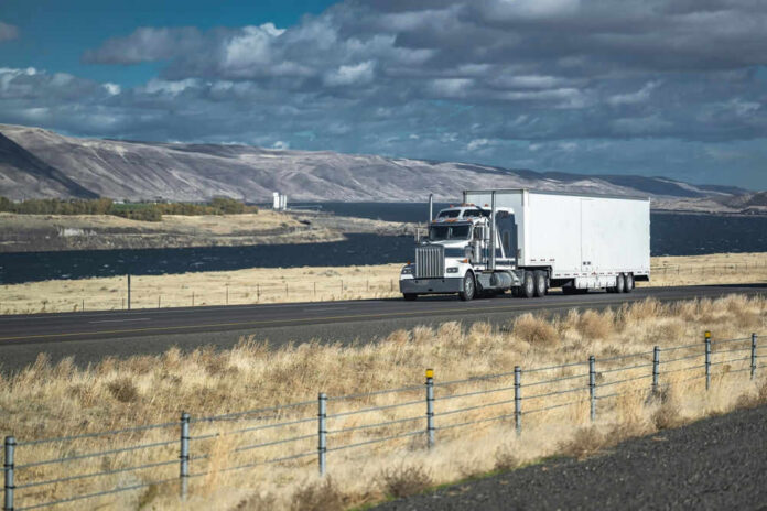 2262168801 Truck driving on rural highway near river and mountains