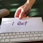 A hand placing an envelope labeled 'I Quit' on a keyboard
