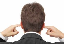 Man in a suit with his hands covering his ears, viewed from the back