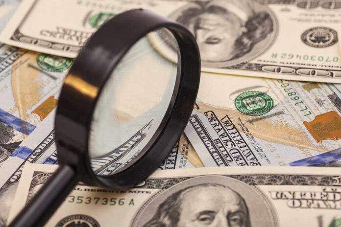A magnifying glass resting on a pile of U.S. dollar bills