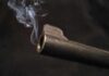 Close-up of a gun barrel emitting smoke against a black background